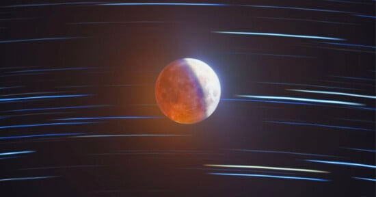 A reddish moon is centered against a dark sky, with streaks of blue and white light creating a sense of motion, resembling star trails during a lunar eclipse.