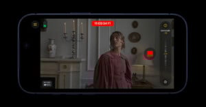 A smartphone screen displays a video recording interface with a woman in a historic-style dress standing near a fireplace, decorative vases, and candlesticks in a vintage room. Exposure settings and a red record button are visible.