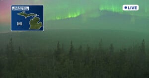 Northern lights glow green in the night sky above a forest at Isle Royale National Park, Michigan. An inset map shows the park's location in Michigan, with a "LIVE" indicator in the upper right corner.