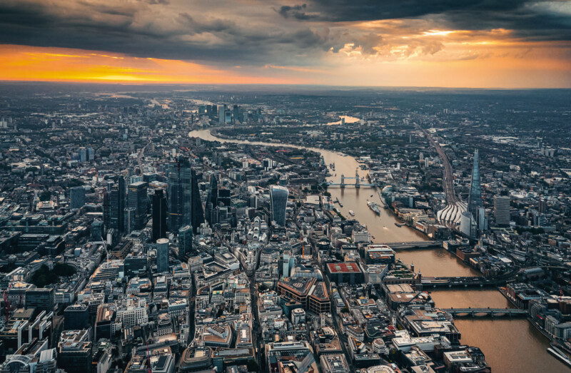 La vista aérea del centro de Londres al atardecer muestra el Támesis que pasa por la ciudad, edificios icónicos como escombros y puentes de torre, visibles bajo un cielo dramático y lleno de nubes.