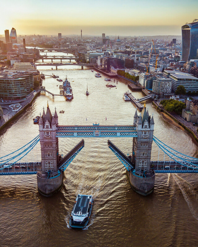 Vista aérea del Puente de la Torre en el Puente de la Torre de Londres, el bote pasa debajo, rodeado de edificios de la ciudad, con un nebuloso cielo al atardecer envuelto en el fondo.