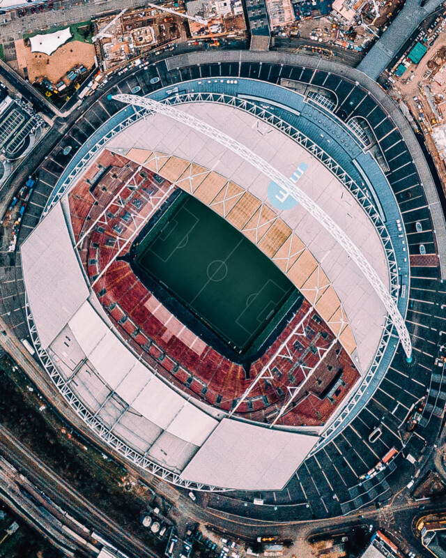 Vista aérea del gran campo de fútbol, ​​asientos verdes y blancos y estructura de techo abovedado. El estadio está rodeado de estacionamientos, carreteras y edificios cercanos.
