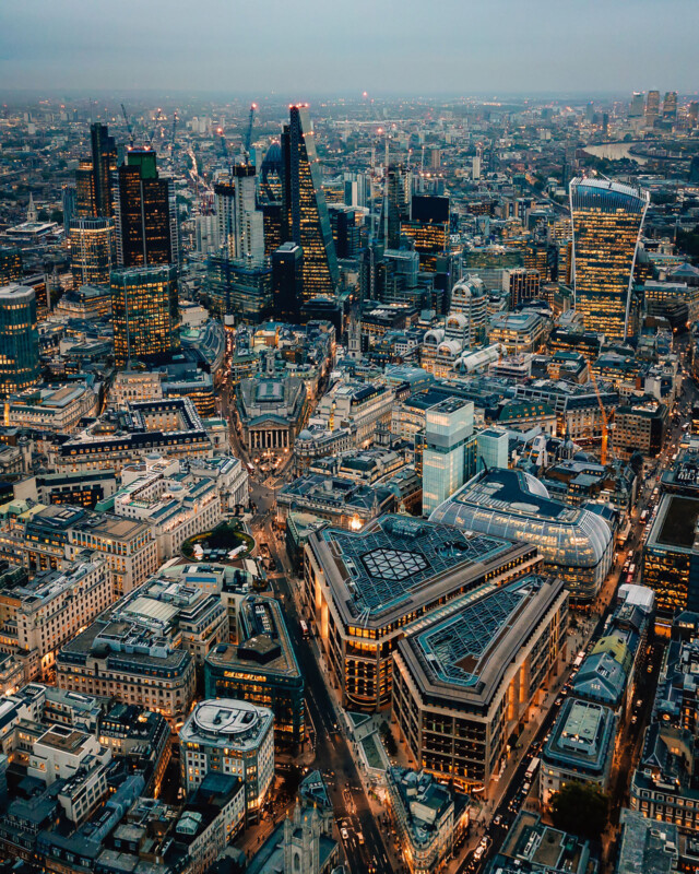 A medida que interviene el anochecer, la vista de pájaros de la ciudad densa con rascacielos modernos, edificios más antiguos, calles concurridas y luces comienzan a iluminar. El paisaje urbano muestra una mezcla de estilo arquitectónico e infraestructura urbana.