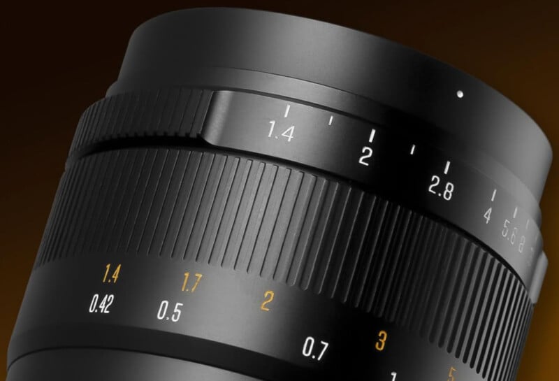 Close-up of a camera lens showing focus and aperture ring markings, including f-stops and distance measurements, against a dark gradient background.