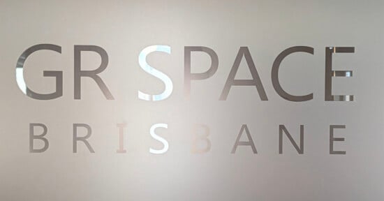 Frosted glass with cut-out letters partially reading "GR SPACE BRISBANE," with the background faintly visible through the transparent text.