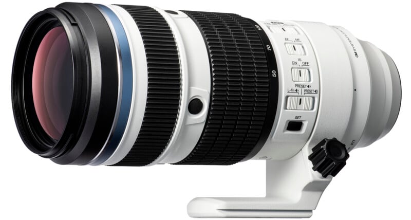 A large white telephoto camera lens with black rubber grip rings, multiple switches, and a tripod mounting collar. The lens has a wide front element and is designed for professional photography.