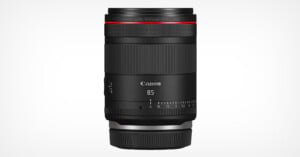 A Canon RF 85mm F1.4 L lens in black, standing vertically against a plain white background. The lens features a red ring near the top and clearly marked focus and aperture settings.