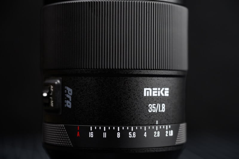 Close-up of a MEKE 35mm f/1.8 camera lens showing focus and aperture markings, a textured grip, and clear white brand and model text on a black background.