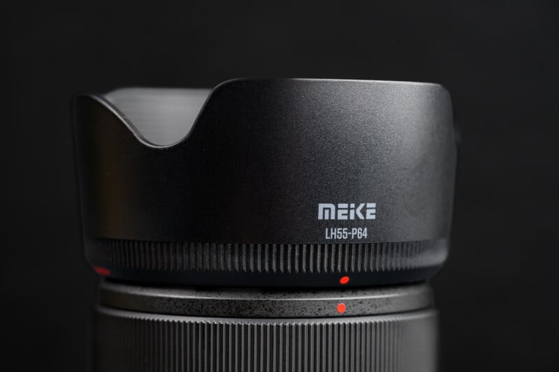Close-up of a MEIKE camera lens with a lens hood attached, showing the model number "LH55-P64" on a matte black surface against a dark background.