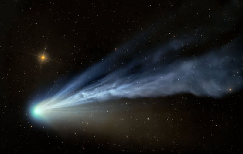A bright comet with a glowing blue-green head and long, wispy tails streams through a star-filled night sky, with a yellow star visible nearby.