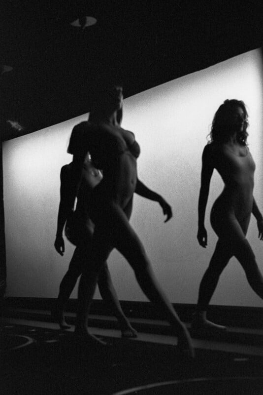 Three people are walking in front of a brightly lit background, their bodies silhouetted in shadow. Their poses suggest motion, and the image has a dramatic, artistic feel with strong contrasts in lighting.