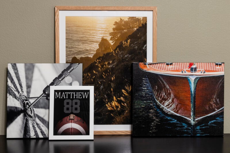 Four framed and unframed prints sit on a dark surface: a sunset over a rocky coastline, a close-up of a wooden boat, a dart hitting a bullseye, and a football-themed card with the name Matthew and the number 88.
