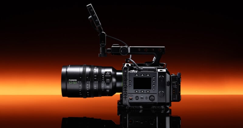 A professional Fujifilm digital cinema camera with a large Fujinon 25-100mm lens and top handle is displayed against a vibrant orange and black gradient background.