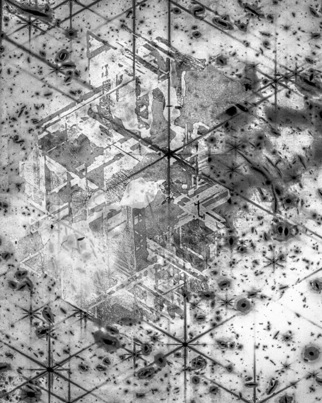 Abstract grayscale image of geometric shapes and grids, featuring a translucent, three-dimensional cube structure layered over a background with scattered dark spots and intersecting lines, creating a complex, textured pattern.