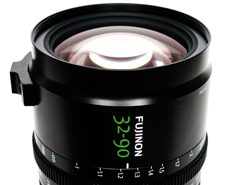 Close-up of a Fujinon 32-90mm camera lens, showing the large front glass element and lens markings in white and green text on a black metal barrel, with focus and aperture adjustment rings.