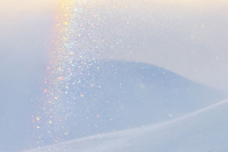 Soft pastel scene of a snowy hill with sunlight creating a subtle rainbow and sparkling effect in the air, giving a dreamy, ethereal atmosphere.