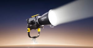 A powerful studio light with the brand name “KNOWLED” emits a bright beam. The light is mounted on a metal stand against a gradient background that fades from dark blue to beige.