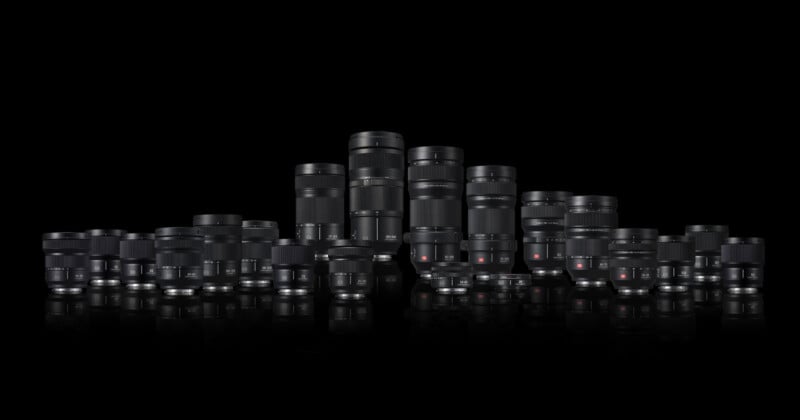 A collection of various camera lenses of different sizes and types arranged in rows against a black background, reflecting slightly on the surface below.