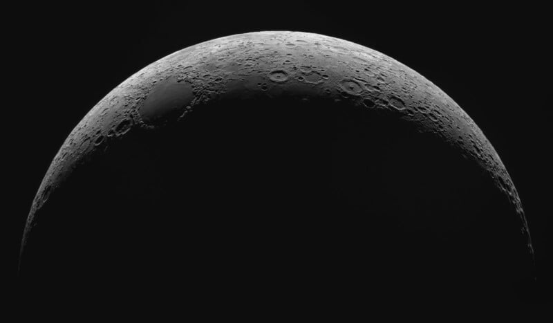 A detailed, high-contrast image of the Moon shows its cratered surface illuminated in a crescent shape against a black background, highlighting the texture and features near the curved edge.