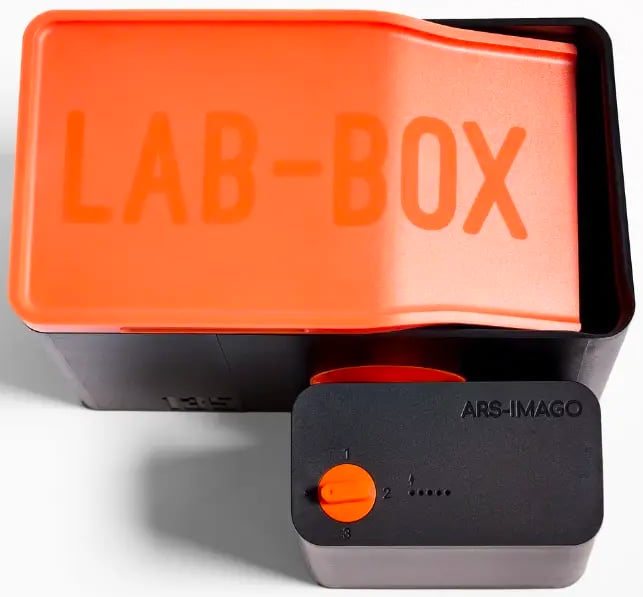 A black and orange film developing tank labeled "LAB-BOX" on the lid, with a dial and the brand name "ARS-IMAGO" visible on the side.