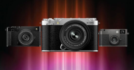 Three digital cameras are displayed side by side against a vibrant, blurred red and purple background, with the central silver and black camera prominently in front.