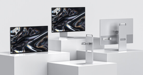 Three modern computer monitors are displayed on white platforms. Two screens show a glossy black abstract pattern, and the third monitor is turned to show its ports and connectors on the back. The setup is minimalist and sleek.