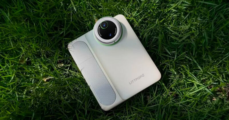 A white Littopo camera with a large circular lens lies on green grass, with sunlight highlighting the texture of both the device and the surrounding blades.