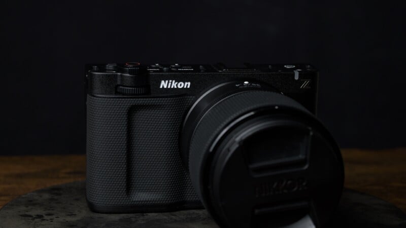 A black Nikon Z series mirrorless camera with a lens attached is placed on a dark surface against a dark background.
