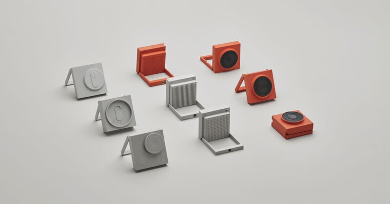 Nine small, square devices in gray and orange are arranged on a light background. Some are open, revealing different textured or patterned interiors, while others are closed or standing upright on fold-out stands.