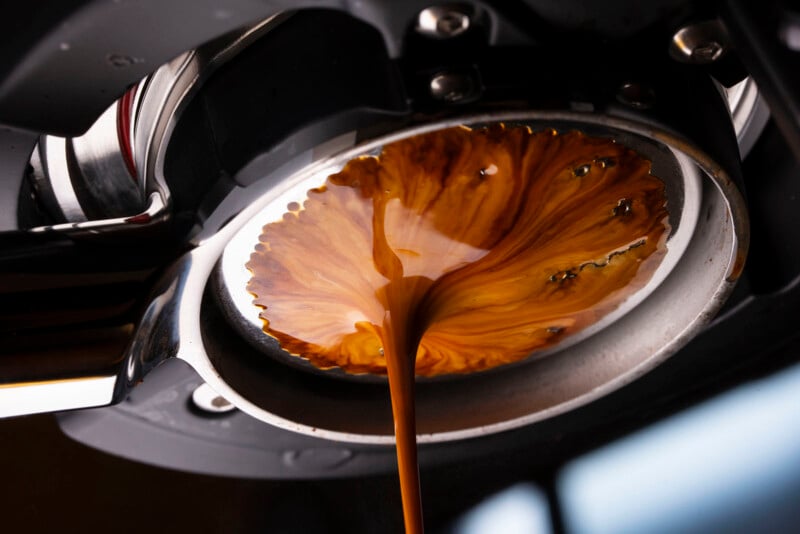 Close-up of espresso flowing from a portafilter, creating a swirling, marbled pattern of rich brown coffee and crema as it pours into a cup below.