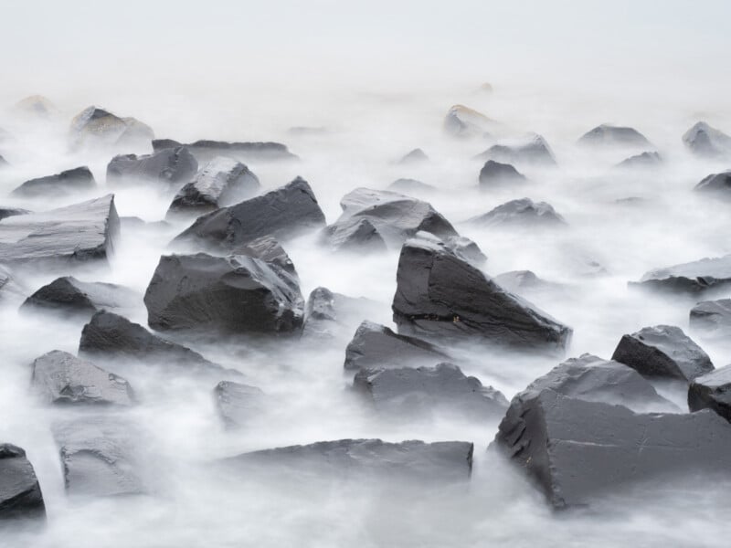 Enormes rocas negras rodeadas de agua brumosa que fluye crean un paisaje costero tranquilo y de ensueño con bordes suaves y una atmósfera serena.