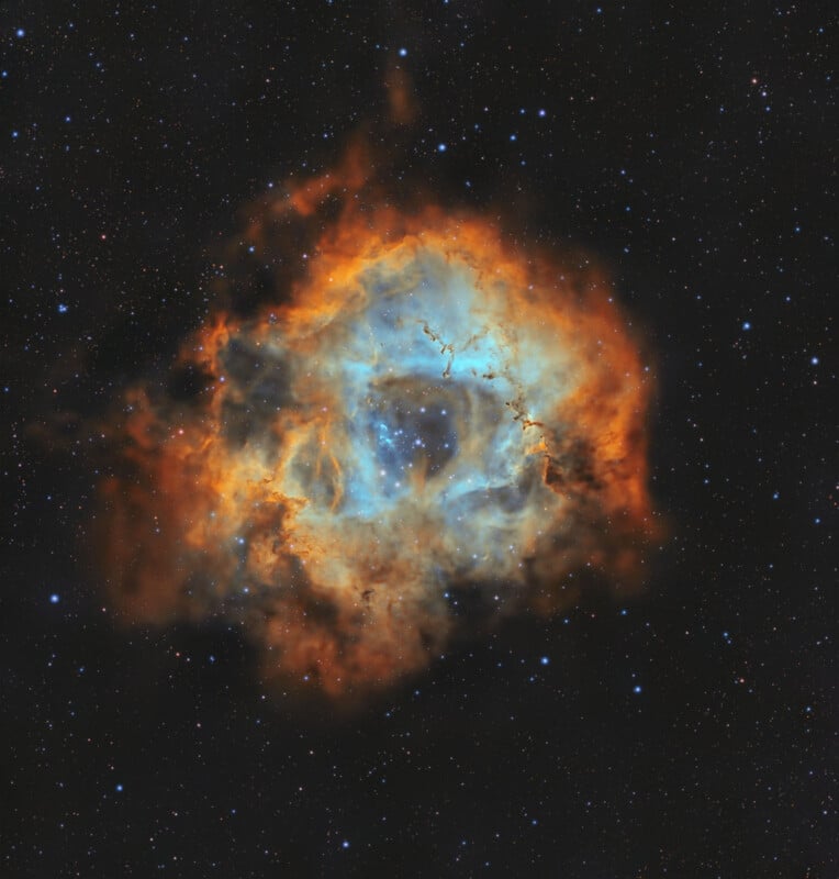 A vivid nebula glows in space with bright blue and orange clouds of gas and dust, surrounded by a backdrop of distant stars on a dark sky.