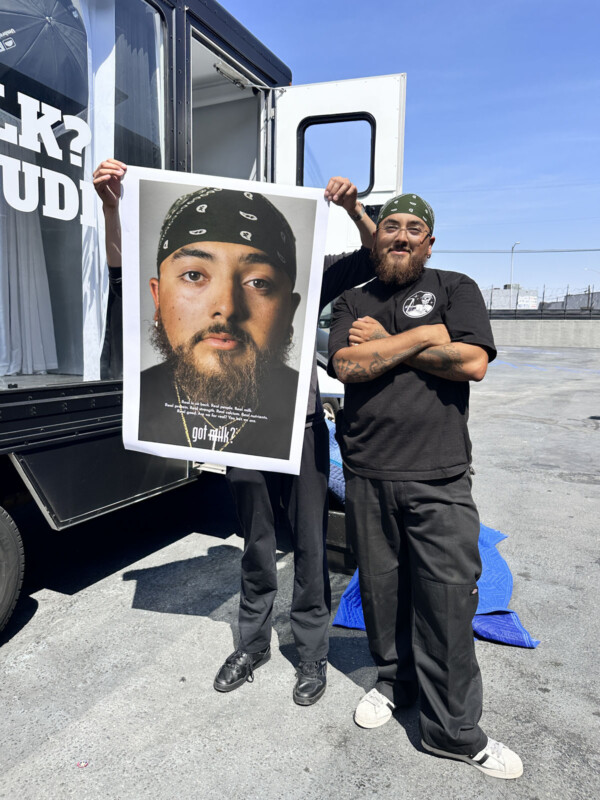 Dos personas se pararon afuera. Un hombre sosteniendo un gran póster de un hombre con un turbante negro y una expresión seria. Otro hombre también llevaba un pañuelo en la cabeza, una camisa negra y pantalones, acercándose a sus brazos junto a él.