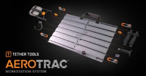 A metallic workstation system with grooves is surrounded by various orange and black mounting accessories. The logo reads "Tether Tools AeroTrac Workstation System" on a dark background.