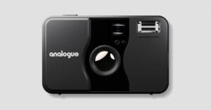 A black analogue film camera with a large lens in the center, a flash in the upper right corner, and the word "analogue" printed in white on the left side. The camera is shown against a plain gray background.