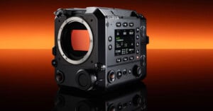A black FUJIFILM digital cinema camera body with a lens mount and control buttons is shown on a reflective surface, against an orange and black gradient background.