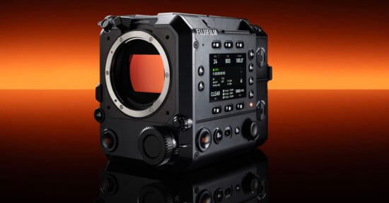 A black FUJIFILM digital cinema camera body with a lens mount and control buttons is shown on a reflective surface, against an orange and black gradient background.