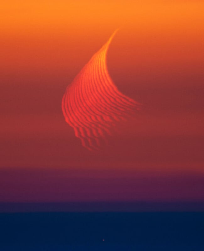 A thin crescent moon appears distorted with wavy patterns against a vibrant orange and purple sunset sky, creating an abstract, dreamy effect.