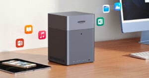 A UGREEN device sits on a wooden desk next to a computer monitor and tablet, with colorful floating icons representing various file types like documents, music, and images above it.