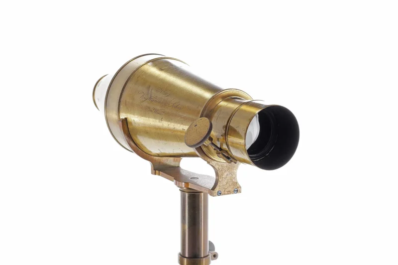 A vintage brass telescope with a cylindrical body mounted on a metal stand, viewed at an angle against a white background.