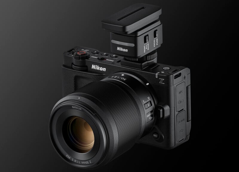A black Nikon Z-series mirrorless camera with a large Nikon lens and an attached external accessory on top, shown against a dark gradient background.