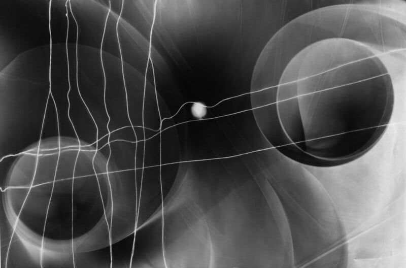Abstract black and white image with overlapping circles, curved and straight white lines, and soft gradients, creating a sense of depth and motion. A small bright sphere appears at the center.