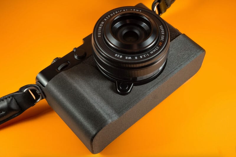 La cámara digital negra de Fuji con lente Fuji se encuentra en bloques rectangulares de espuma negra en un fondo naranja brillante. La cámara viene con un cinturón negro.
