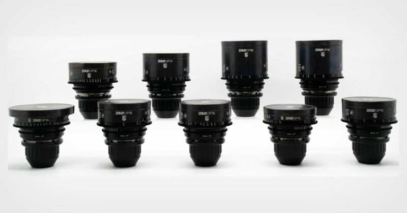Nine black camera lenses of varying sizes are arranged in two rows against a plain white background, showcasing their different focal lengths and aperture markings.