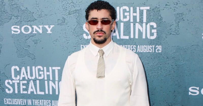 A man with curly hair, a beard, and sunglasses stands in front of a step-and-repeat backdrop for "Caught Stealing." He is wearing a white shirt, ivory vest, and a striped tie. The event is promoted by Sony.
