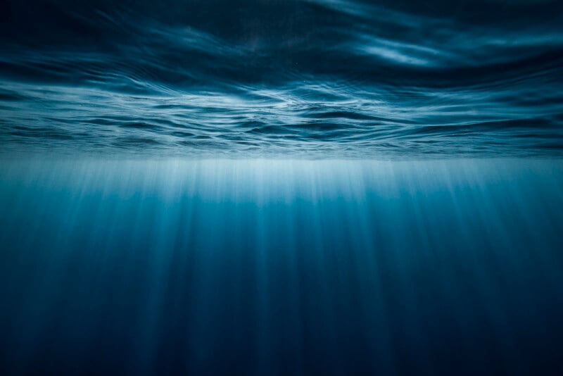 Underwater view looking up toward the ocean surface, with sunlight filtering through the water, creating blue rays and a peaceful, serene atmosphere.