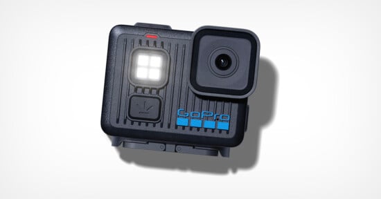 A black GoPro action camera with a prominent lens, built-in LED display, and blue GoPro logo is shown on a white background. The camera casts a soft shadow.