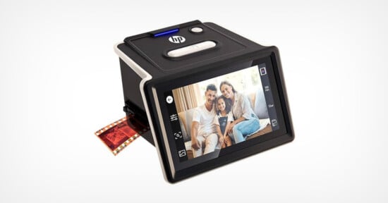 A black HP digital scanner displays a family photo on its screen while scanning a strip of photographic film, with the film partially inserted into the device.