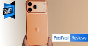 A hand holds an orange iPhone with dual cameras. The Petapixel Editors’ Choice badge is on the left, and the Petapixel Reviews logo is on the right against a beige background.