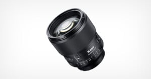 A black Kase camera lens is shown angled on a white background, featuring focus and aperture rings, with visible lens glass and markings for aperture settings.